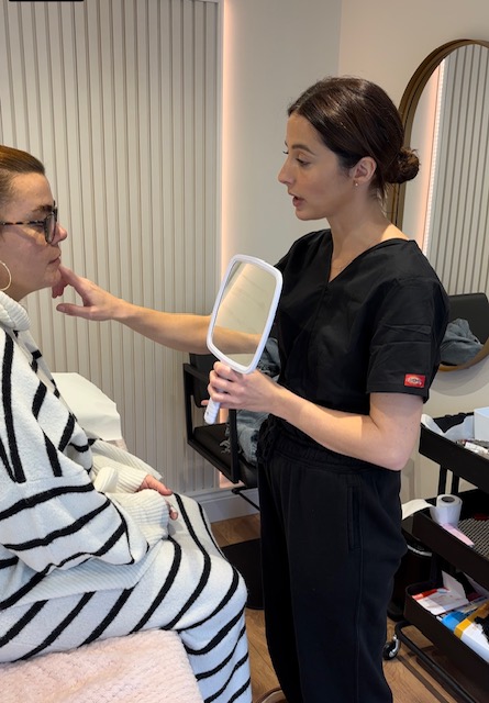 Sarah holding mirror up to a client, who sits on a treatment bed in a salon.