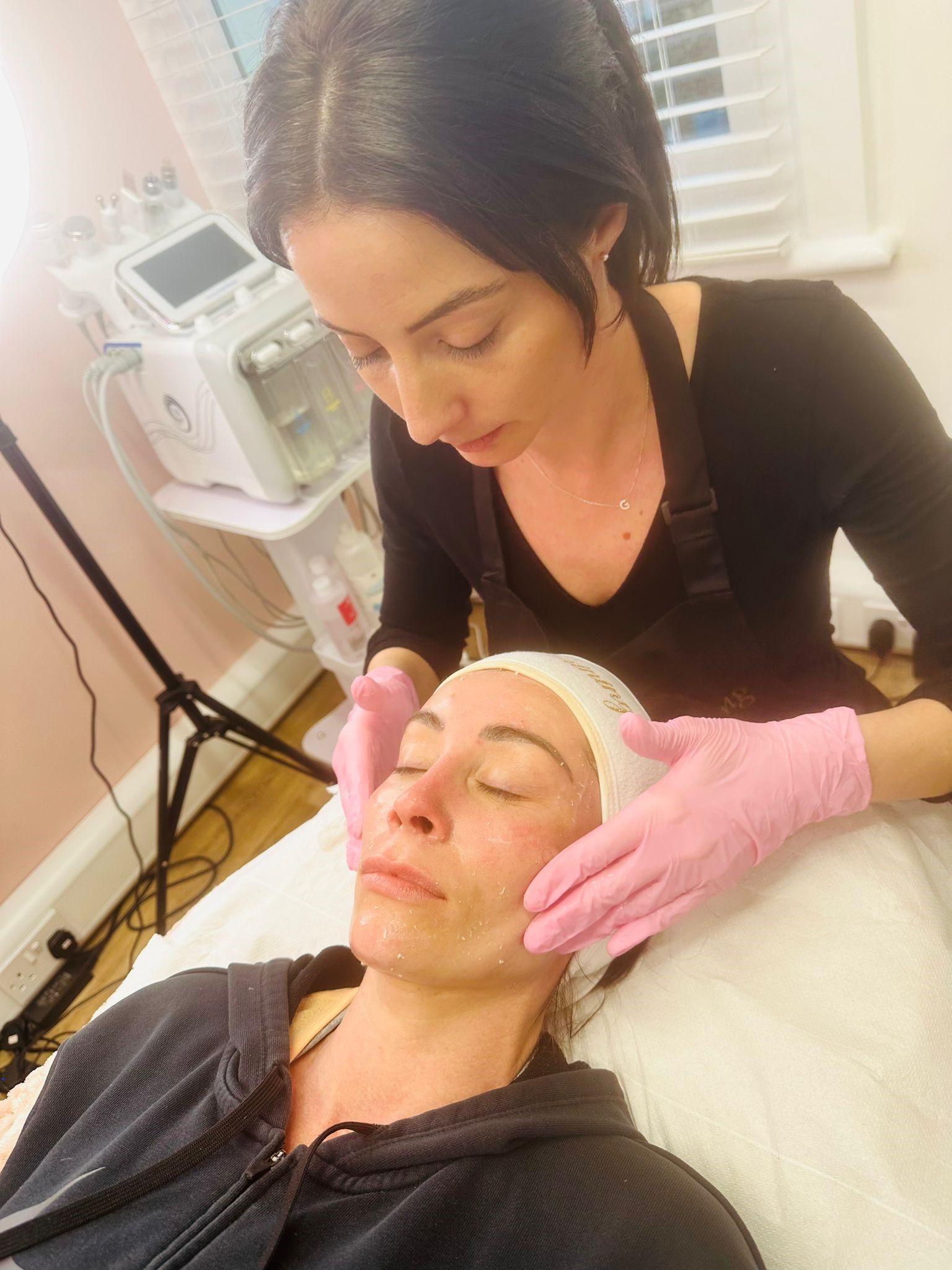 Sarah applying cream to a woman's face during a facial.