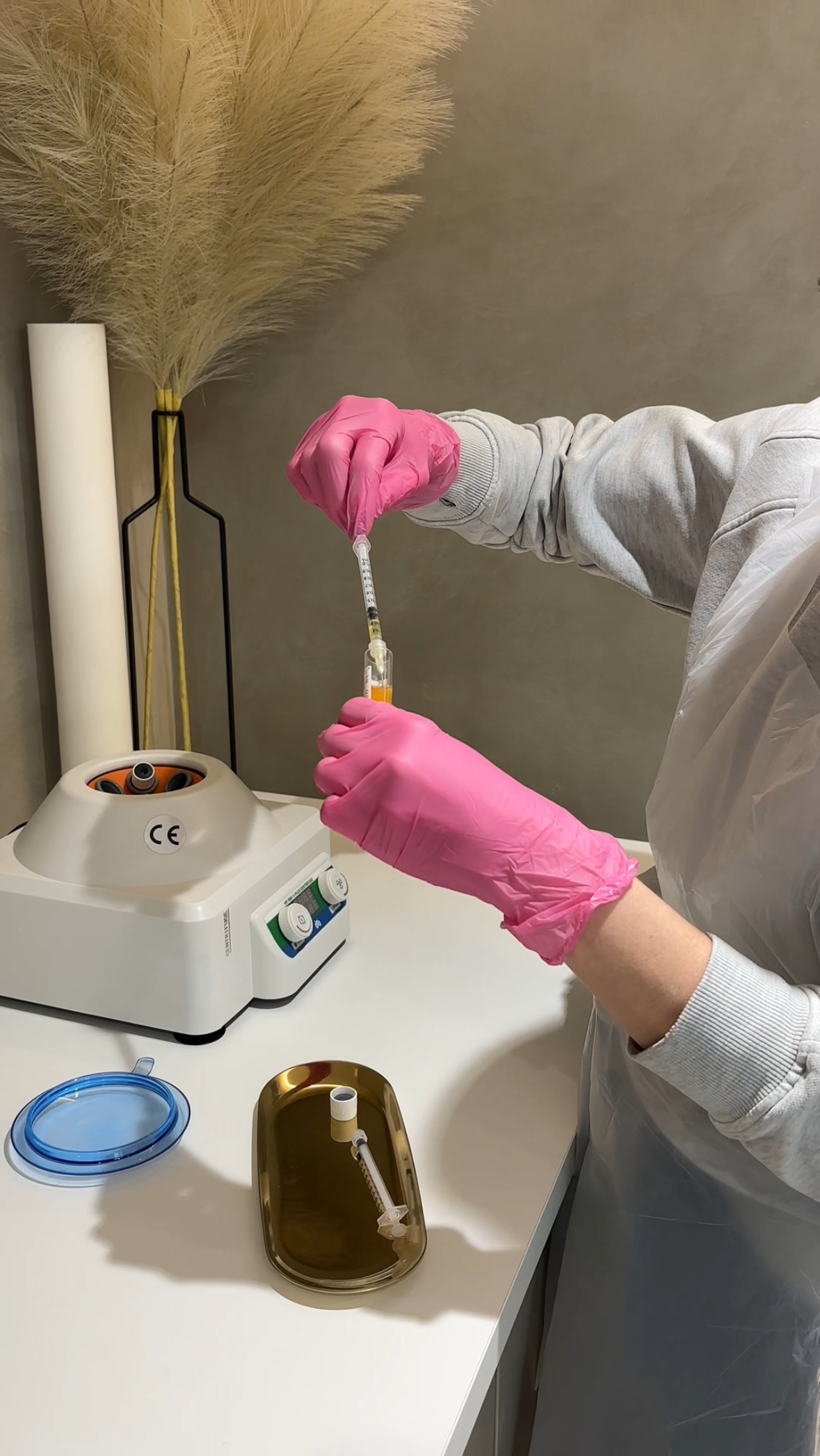 Pink gloved hands holding a vial of blood over a centrifuge. 